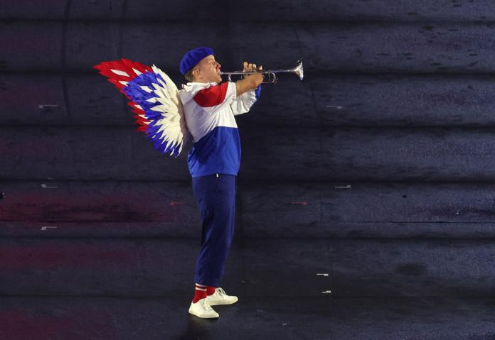 A trumpet player dressed in red white and blue, with feathers on his back and a blue hat, plays the French national anthem